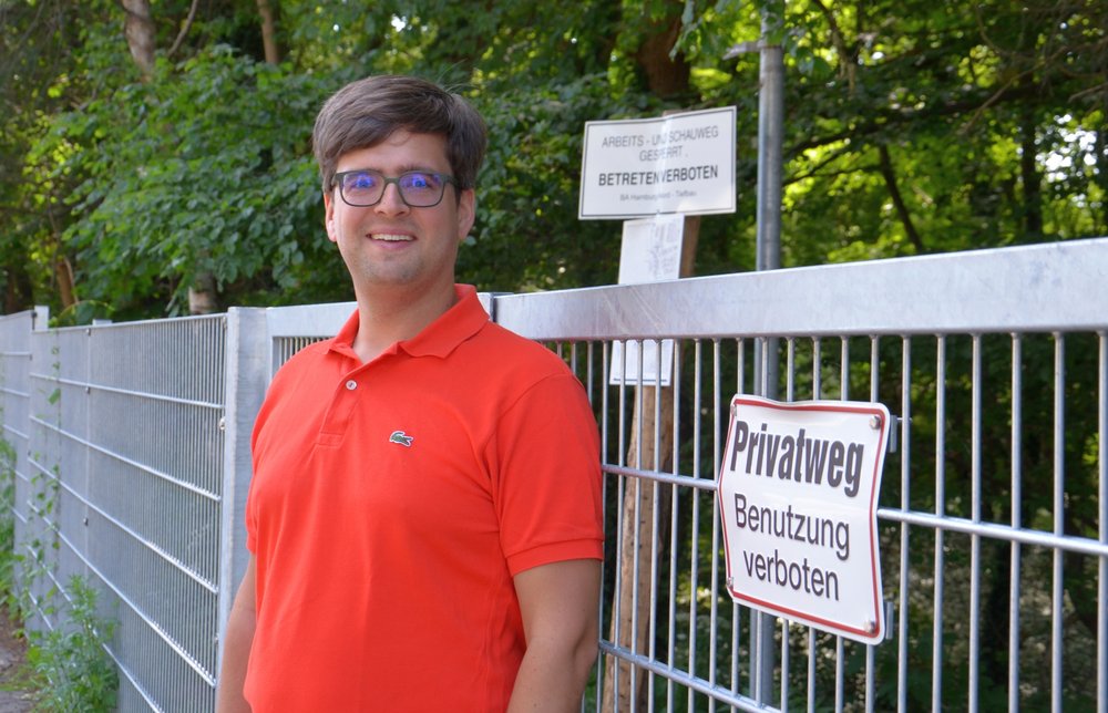 Timo B. Kranz (GRÜNE) am Tor, das derzeit noch in der Straße Tarpen den Weg am Bachufer versperrt
