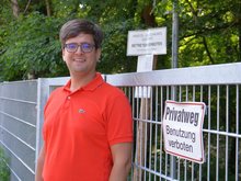 Timo B. Kranz (GRÜNE) am Tor, das derzeit noch in der Straße Tarpen den Weg am Bachufer versperrt